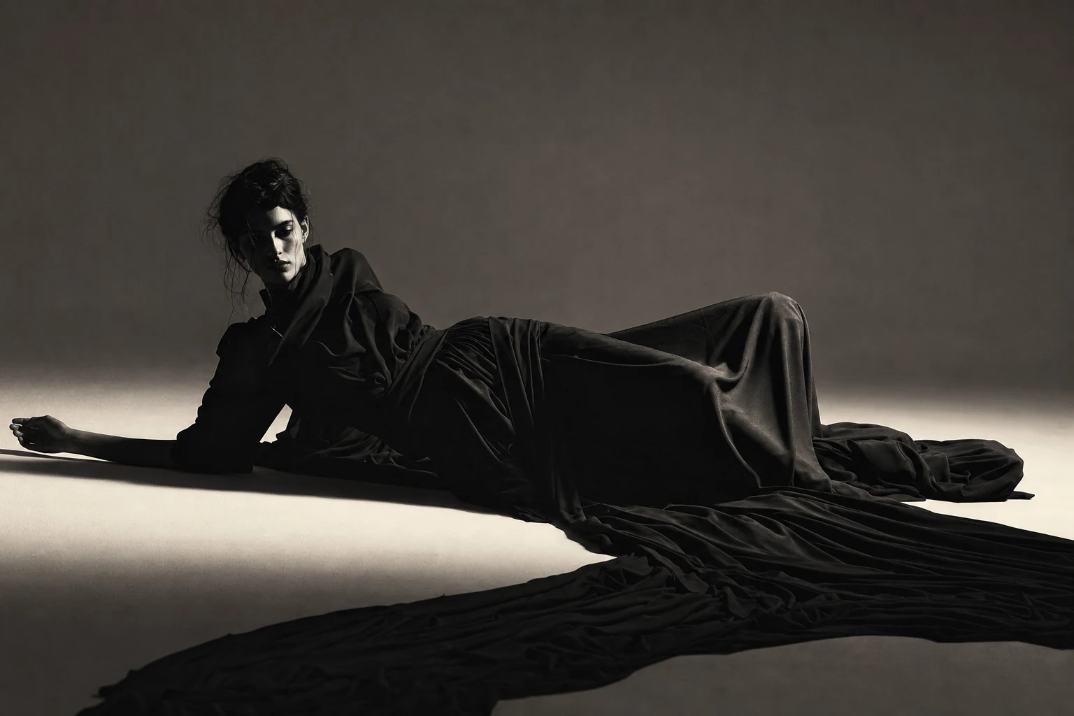 Look III — a model reclining, wrapped in yards of matte black silk crepe pooling across a pale floor.